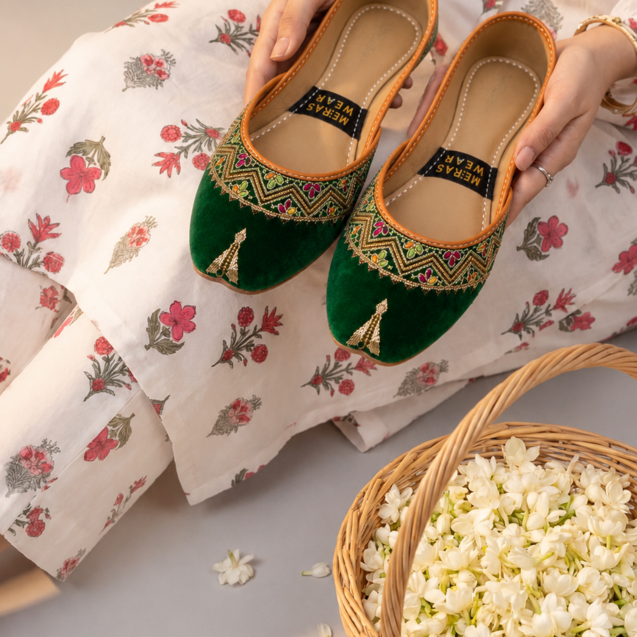 Green velvet embroidered khussa pair held in hands with a floral traditional outfit.